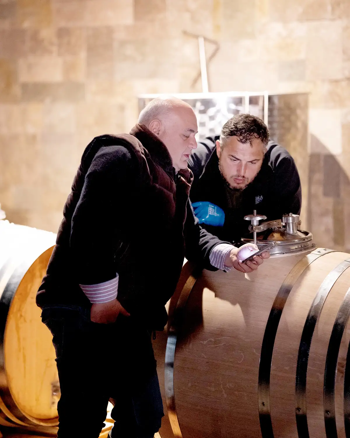 Irakli Gilauri and Guram Gabelaia examine data together in a winery setting, leaning over a cask of Saperavi, the celebrated Georgian wine variety.