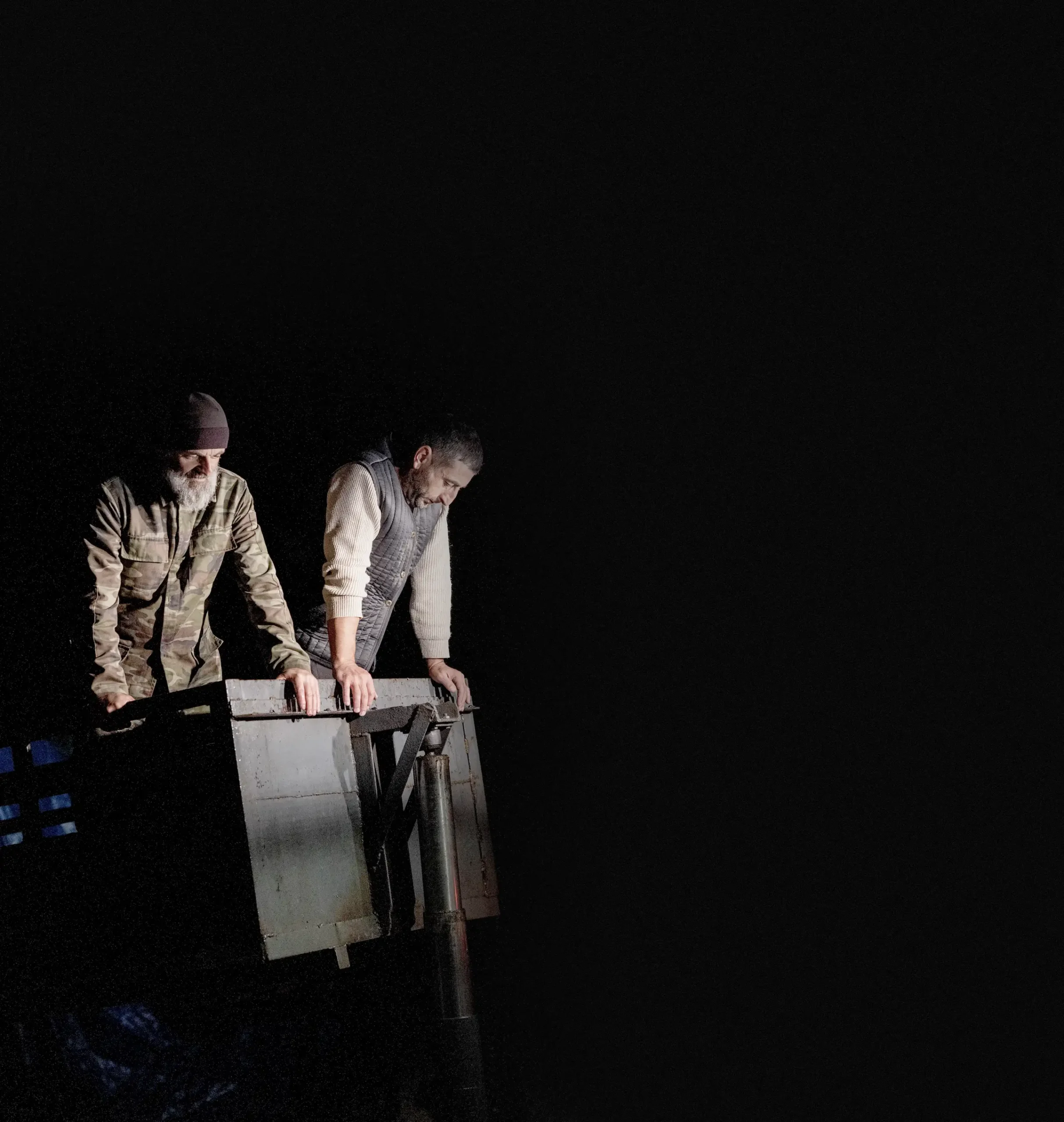 Two men stand leaning over the edge of a piece of winemaking equipment, illuminated against a dark background at night in Kakheti, Georgia.